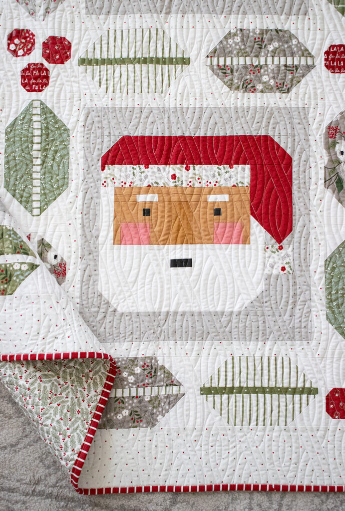 St. Nick quilt in Christmas Eve fabric by Lella Boutique for Moda Fabrics. Cute Santa quilt made with a jelly roll, framed in holly and berry leaf units. Download the PDF here!