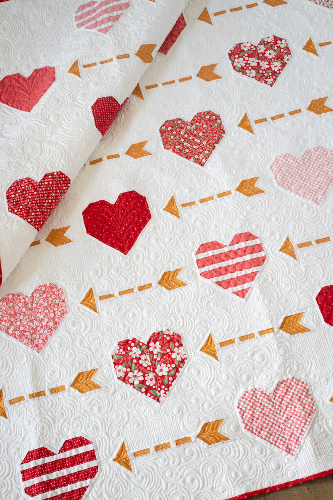 "Playing Cupid" heart and arrow quilt by Vanessa Goertzen of Lella Boutique. Cute Layer Cake valentines quilt! Fabric is Love Blooms by Lella Boutique for Moda Fabrics (Nov 2024).