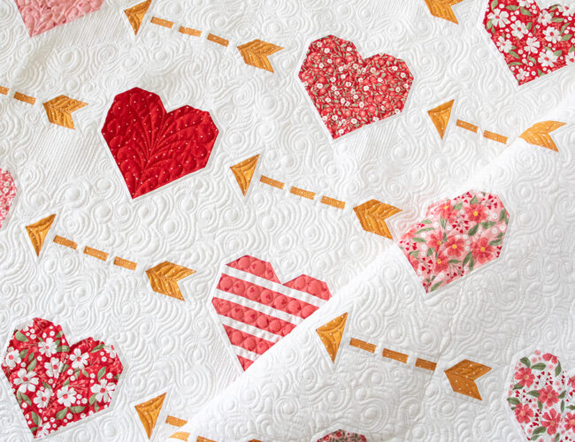 "Playing Cupid" heart and arrow quilt by Vanessa Goertzen of Lella Boutique. Cute Layer Cake valentines quilt! Fabric is Love Blooms by Lella Boutique for Moda Fabrics (Nov 2024).
