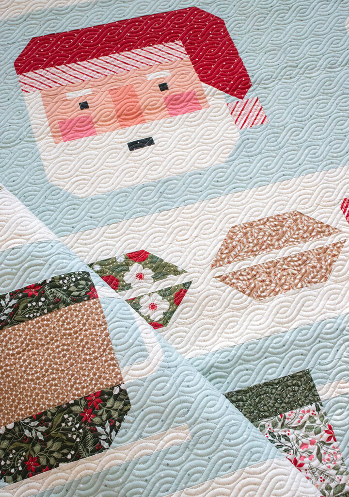 "Cocoa Party" Christmas row quilt by Vanessa Goertzen of Lella Boutique. Sampler includes patchwork Santa, cocoa mugs, marshmallows, and holly berry sashing. Fabric is Peppermint Cocoa by Lella Boutique for Moda Fabrics Download the PDF here!