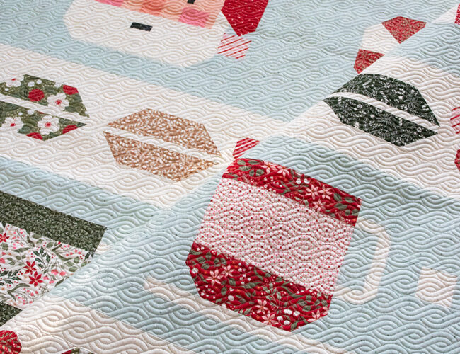 "Cocoa Party" Christmas row quilt by Vanessa Goertzen of Lella Boutique. Sampler includes patchwork Santa, cocoa mugs, marshmallows, and holly berry sashing. Fabric is Peppermint Cocoa by Lella Boutique for Moda Fabrics Download the PDF here!