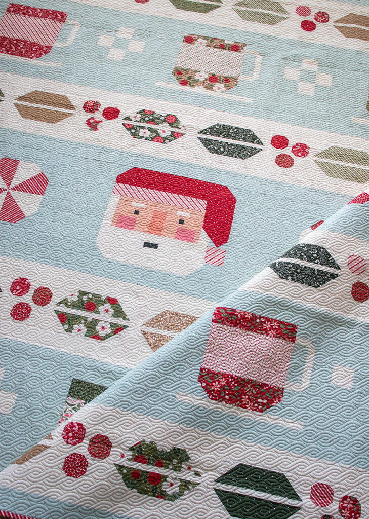 "Cocoa Party" Christmas row quilt by Vanessa Goertzen of Lella Boutique. Sampler includes patchwork Santa, cocoa mugs, marshmallows, and holly berry sashing. Fabric is Peppermint Cocoa by Lella Boutique for Moda Fabrics Download the PDF here!